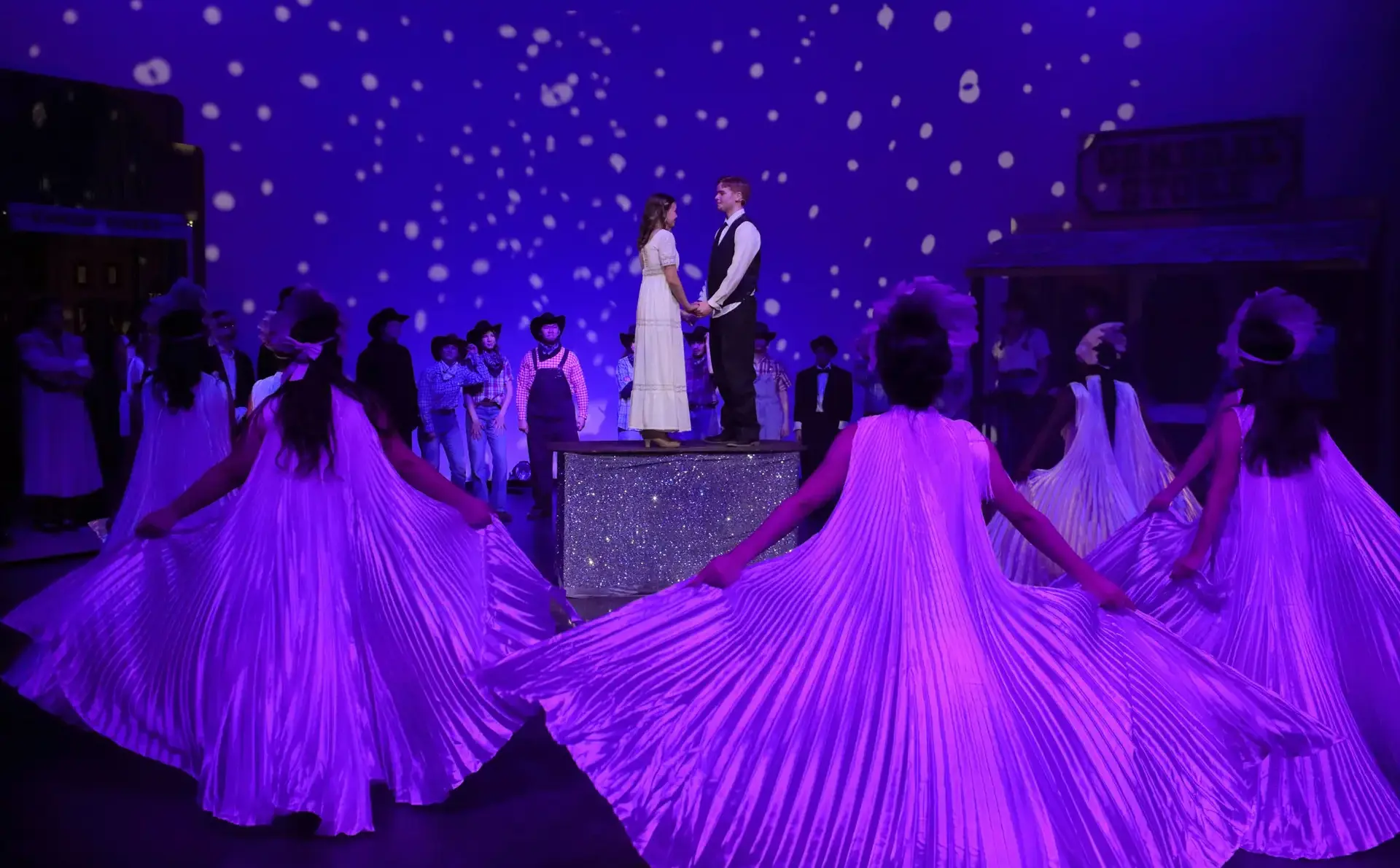 Students performing onstage, bathed in purple light