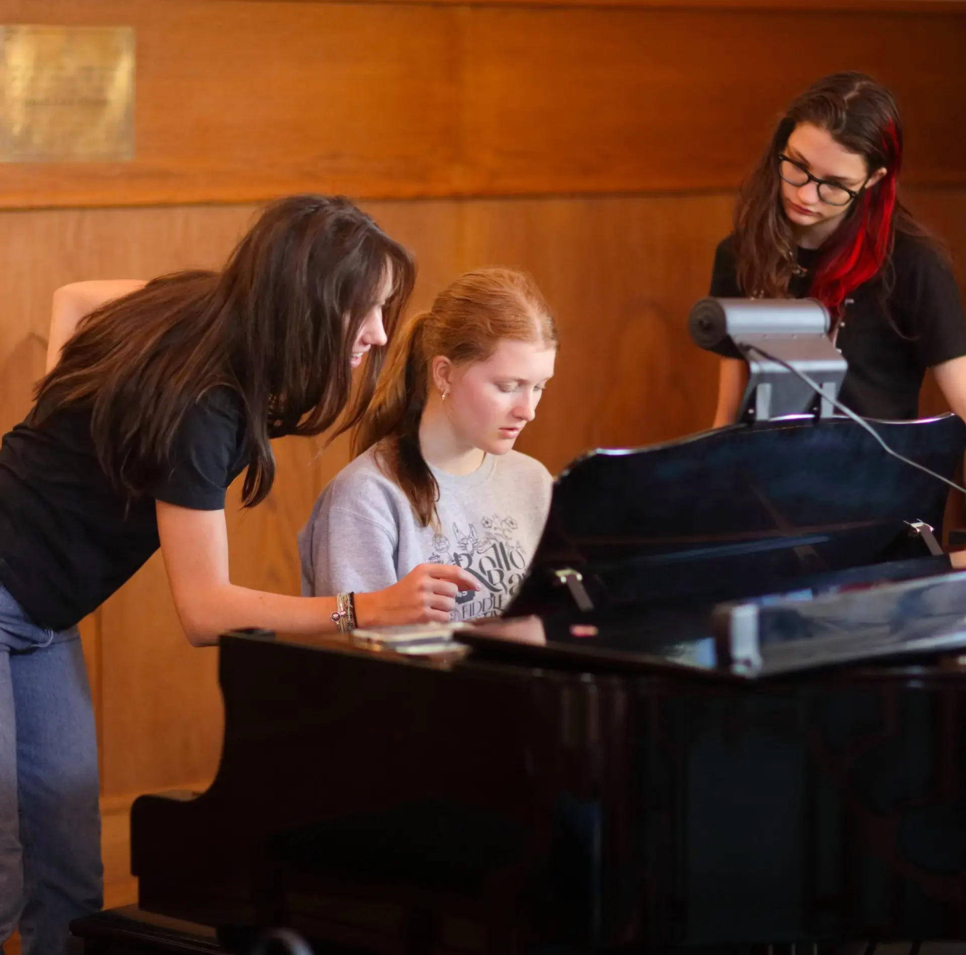 Students looking over sheet music, sitting at piano