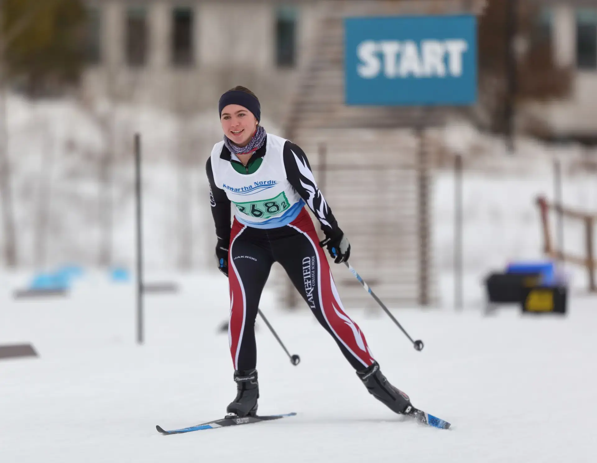A student wearing a Lakefield College School racing suit and a 'Kawartha Nordic' bib competes in a cross-country ski race.