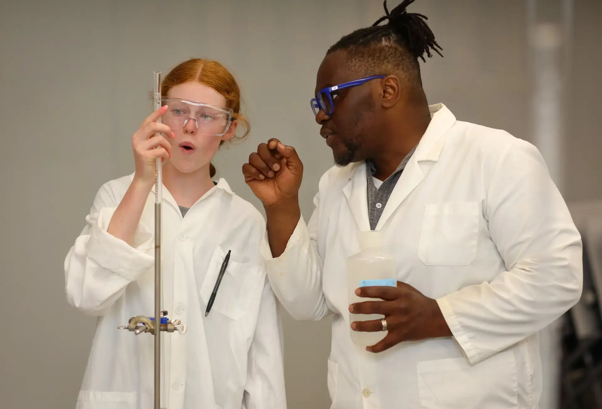 Student and teacher performing experiment, wearing lab gear