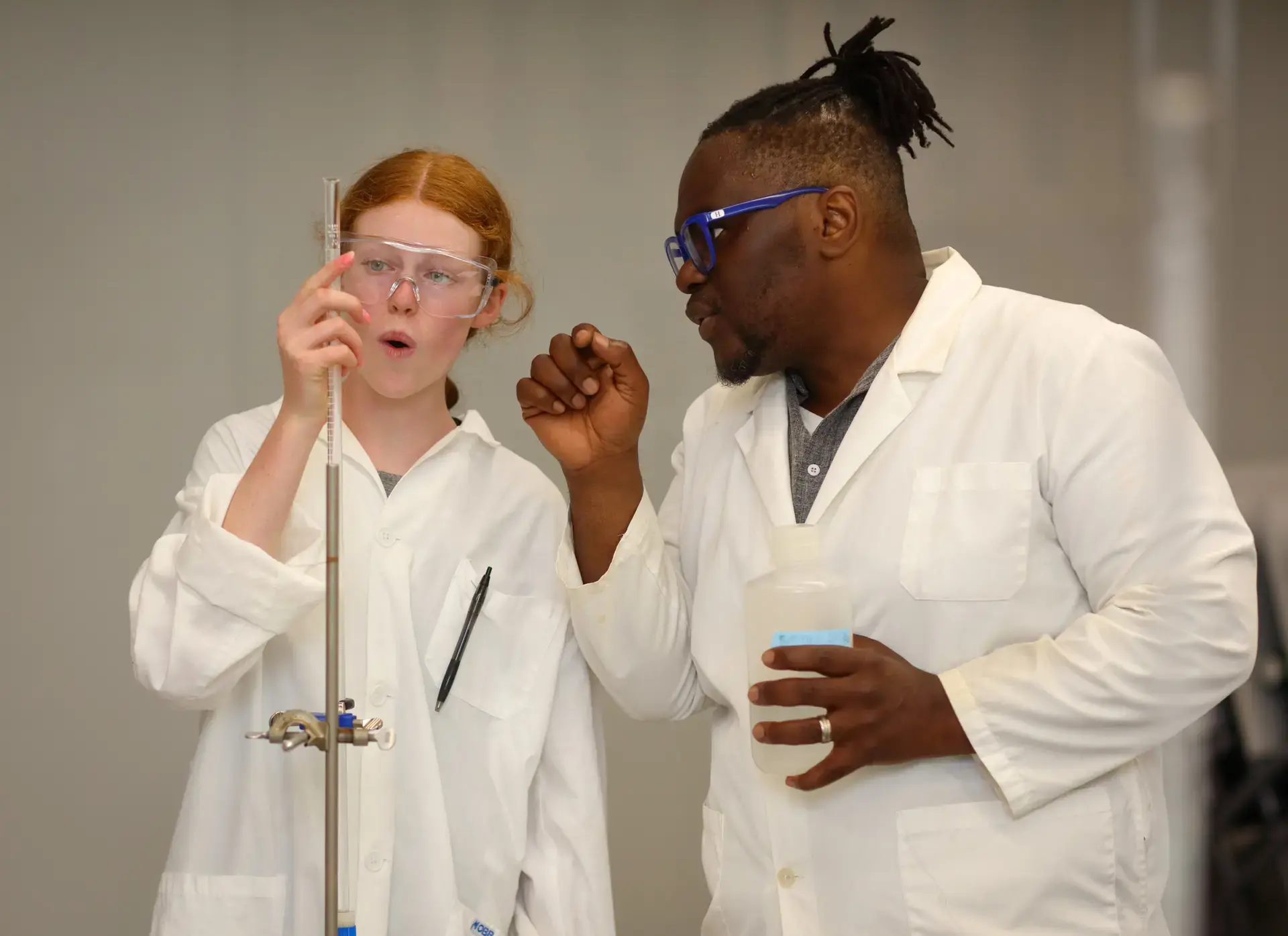 Teacher and student wearing lab gear, performing experiment
