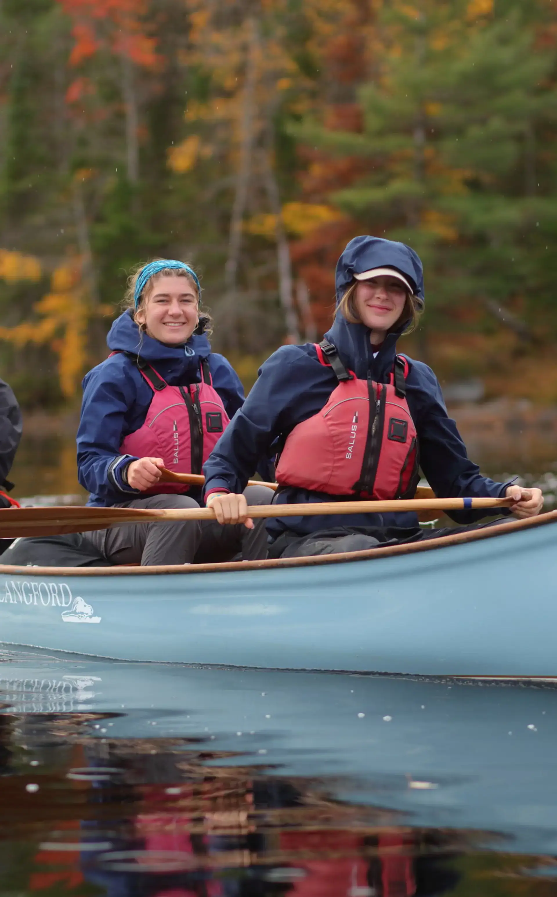 Two students in a canoe smiling at the camera with a lush forest backdrop