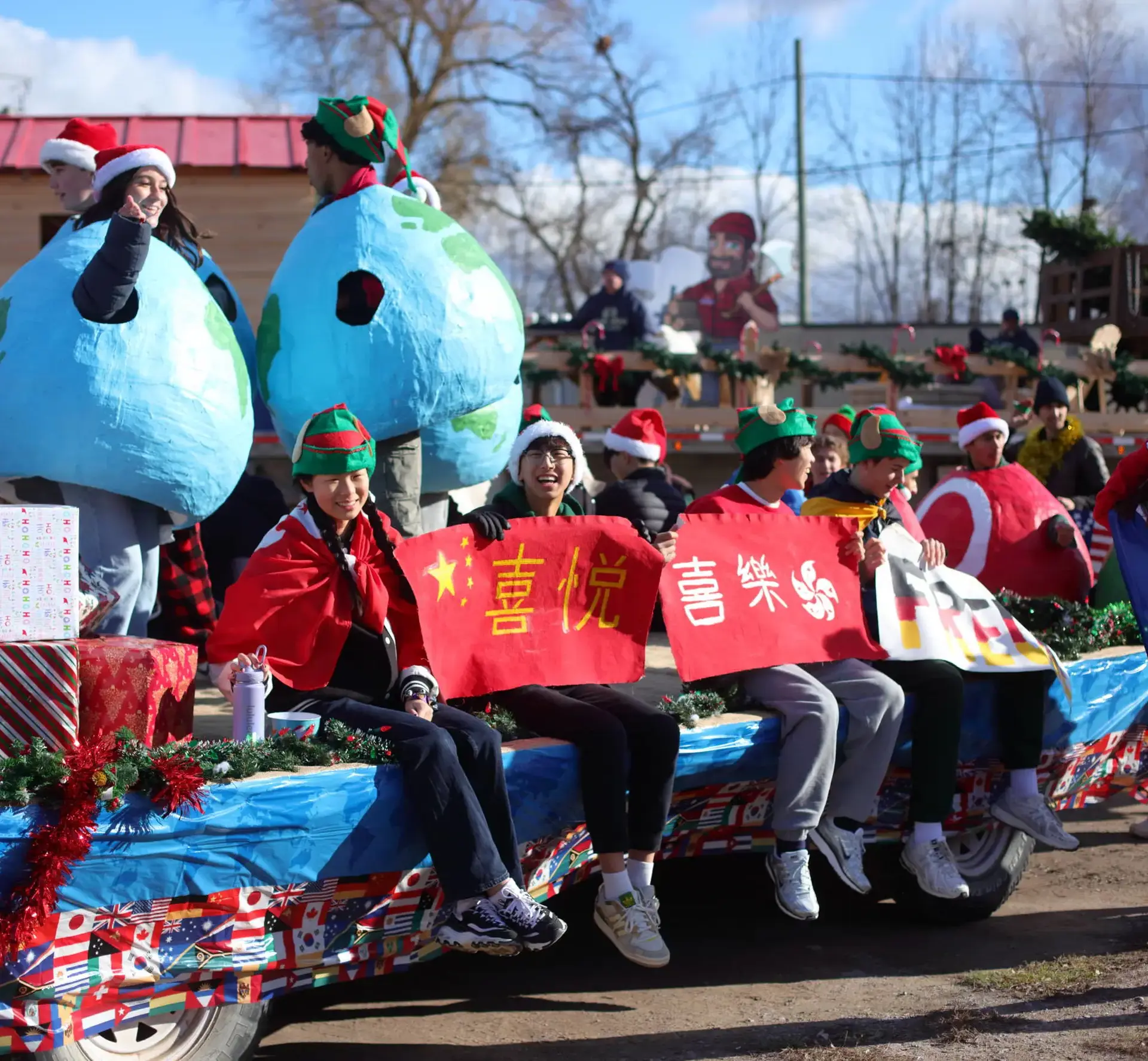 A group of students in holiday costumes and festive attire riding on a parade float decorated with international flags and giant globes.