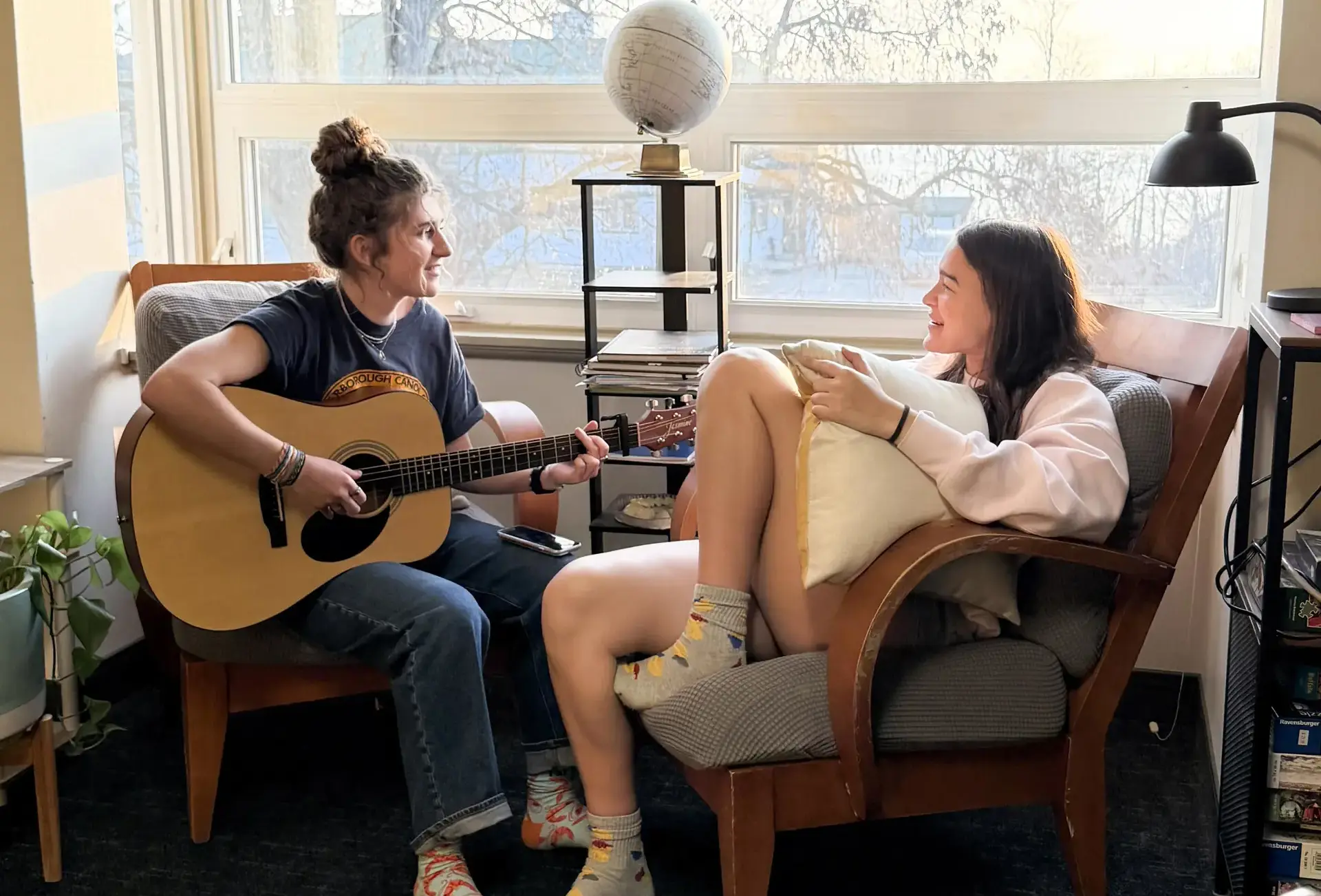 Two students sitting in comfy chairs, one holding an acoustic guitar
