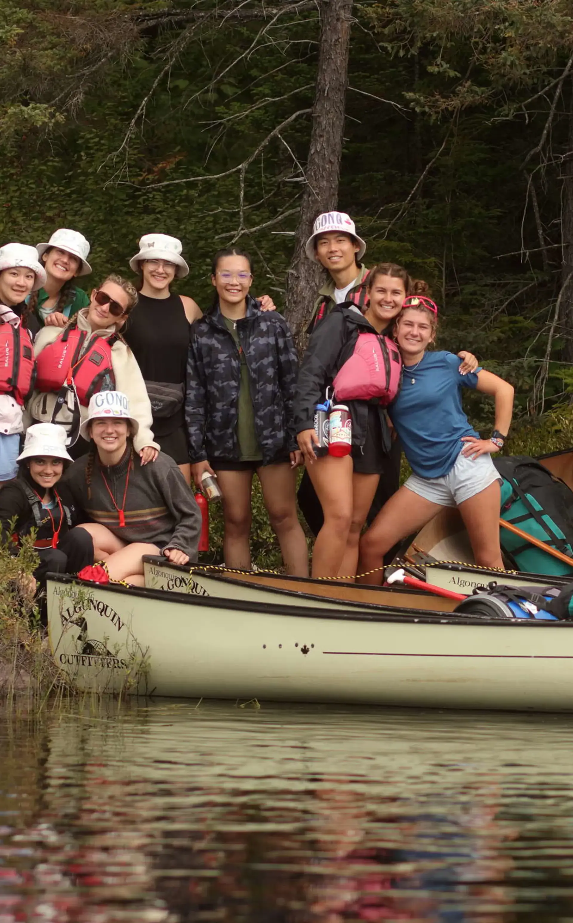 Students wearing hats, smiling from canoes