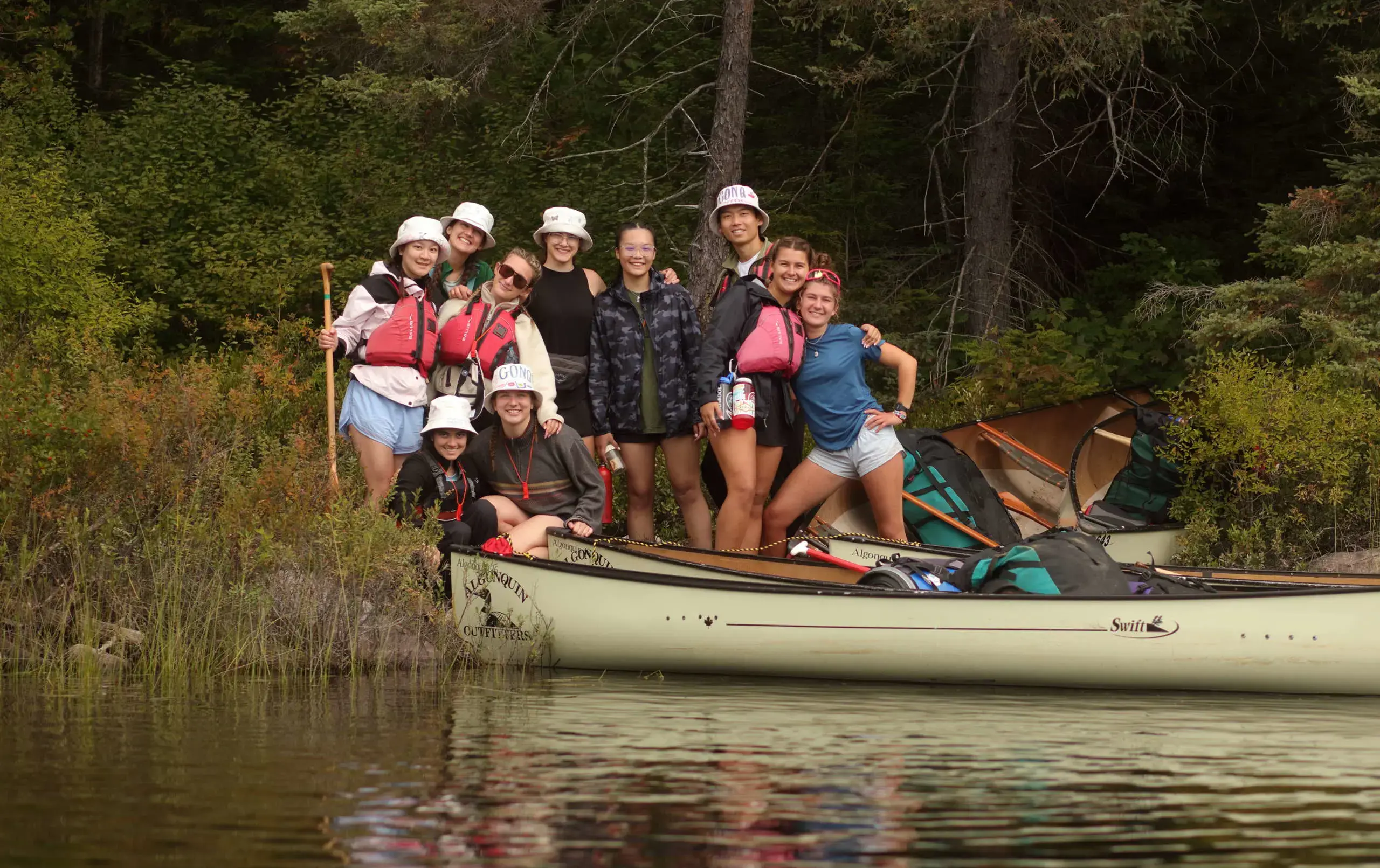 Students standing on bank of lake, wearing white hats