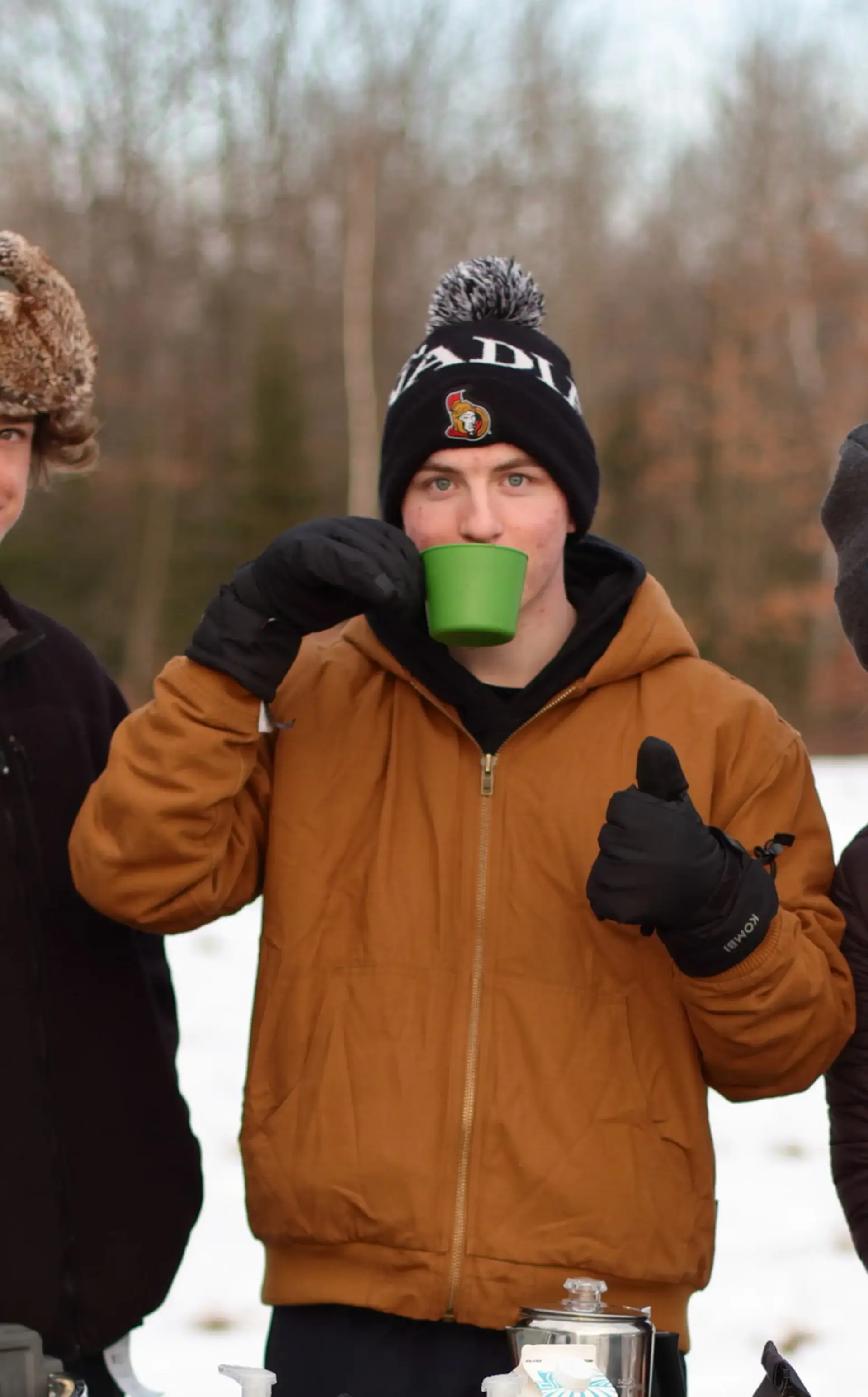 Three students standing together, one drinking from a mug