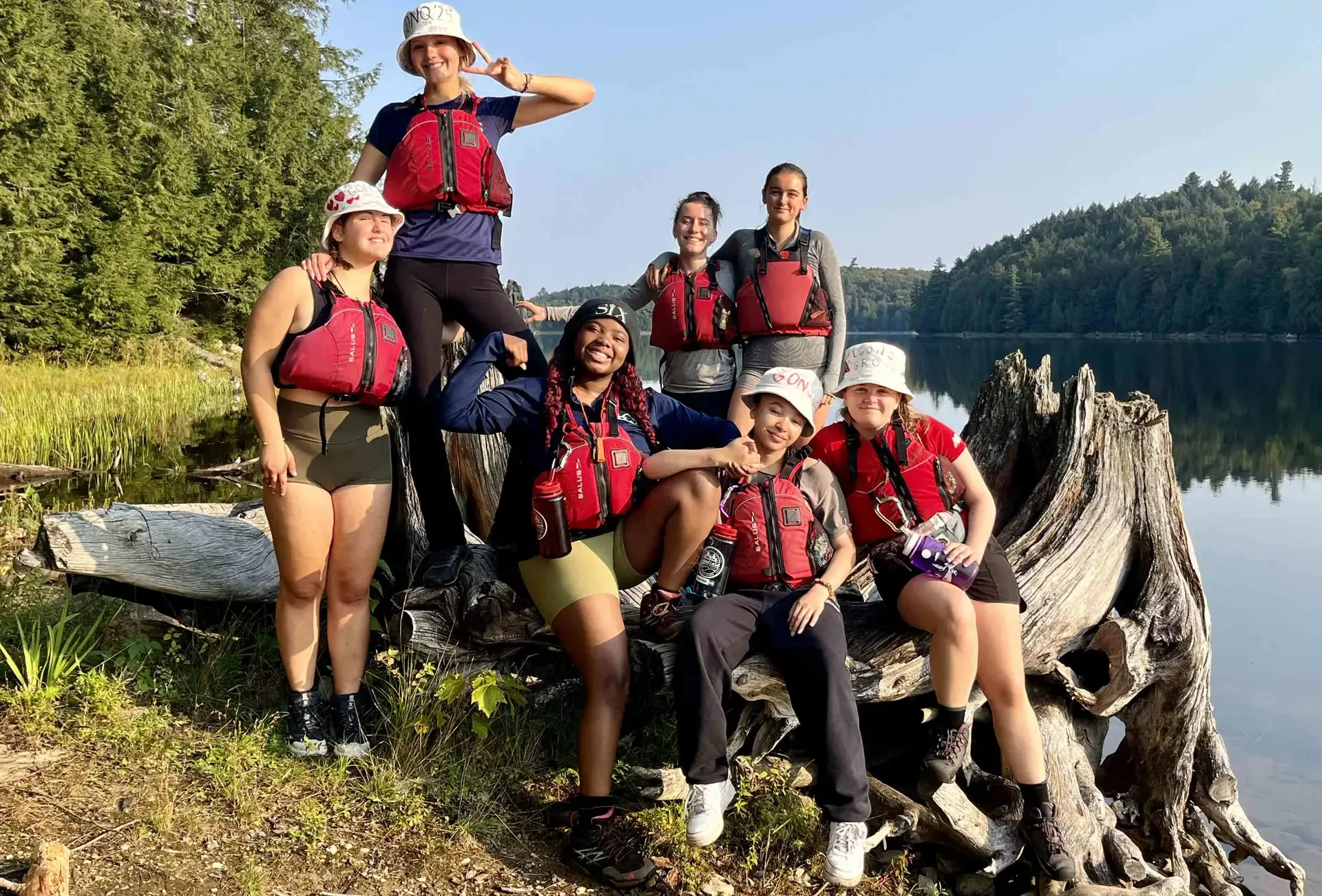 Students wearing boating gear, sitting by lake