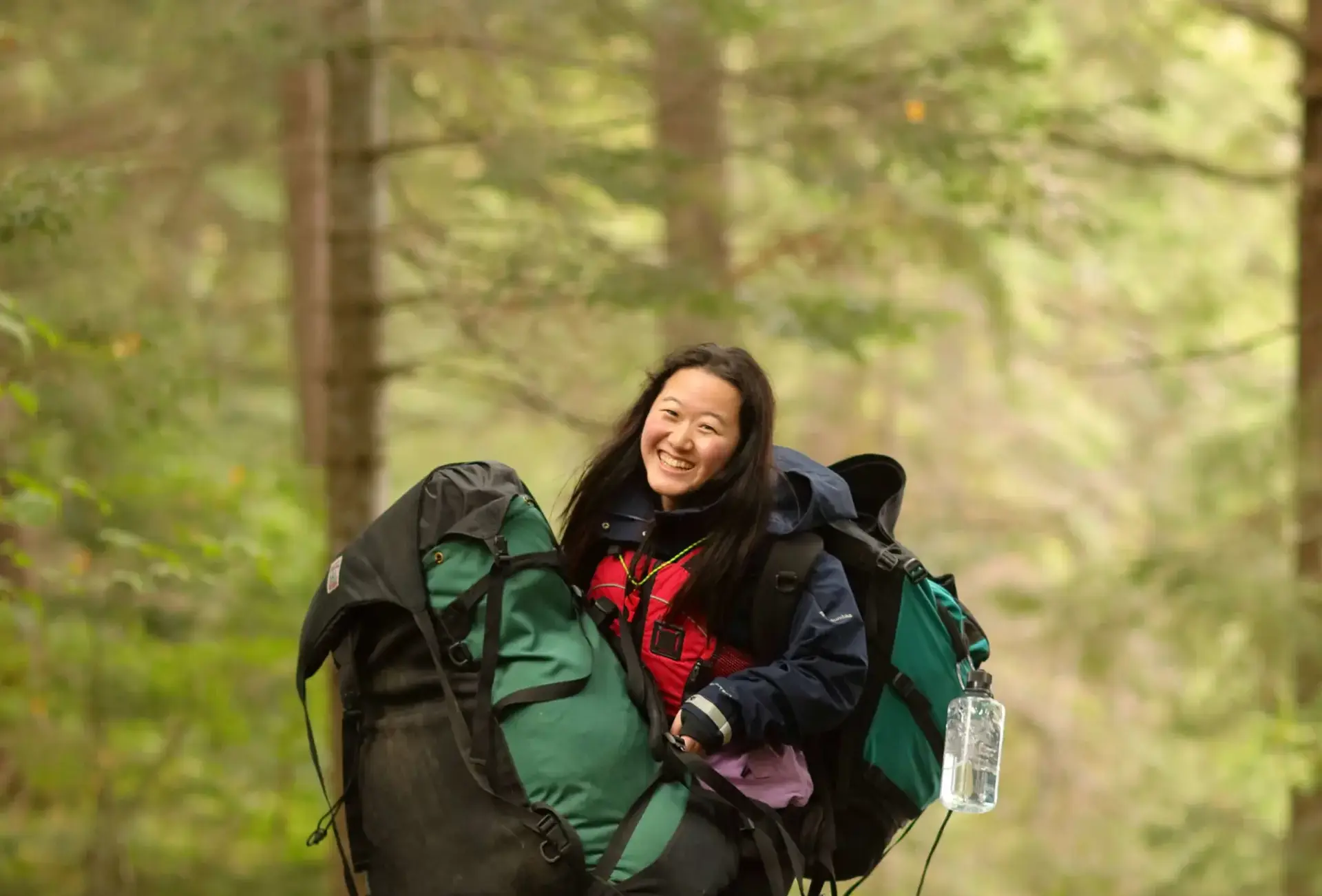 Student standing in forest holding rucksacks
