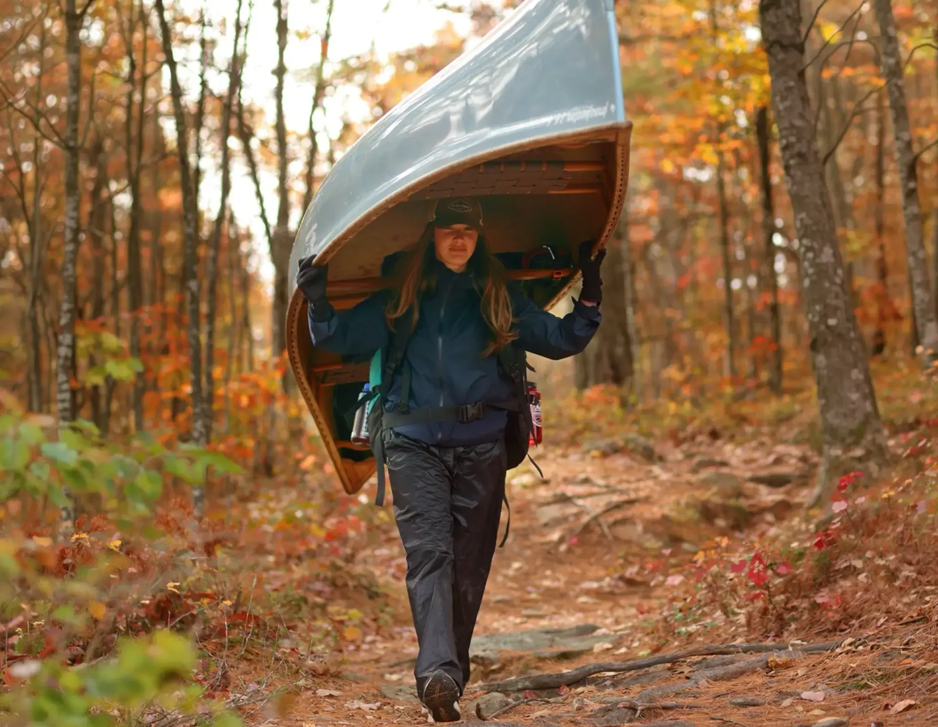 Student portaging canoe through the woods trails
