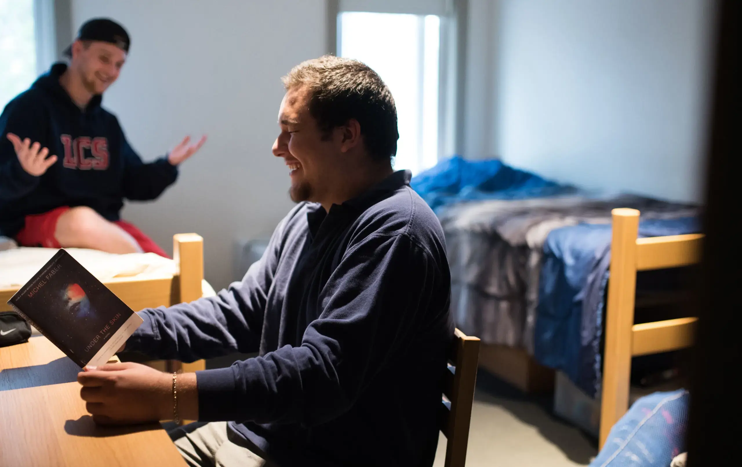 Two students hanging out in dorm room, one reading Under the Skin by Michel Faber