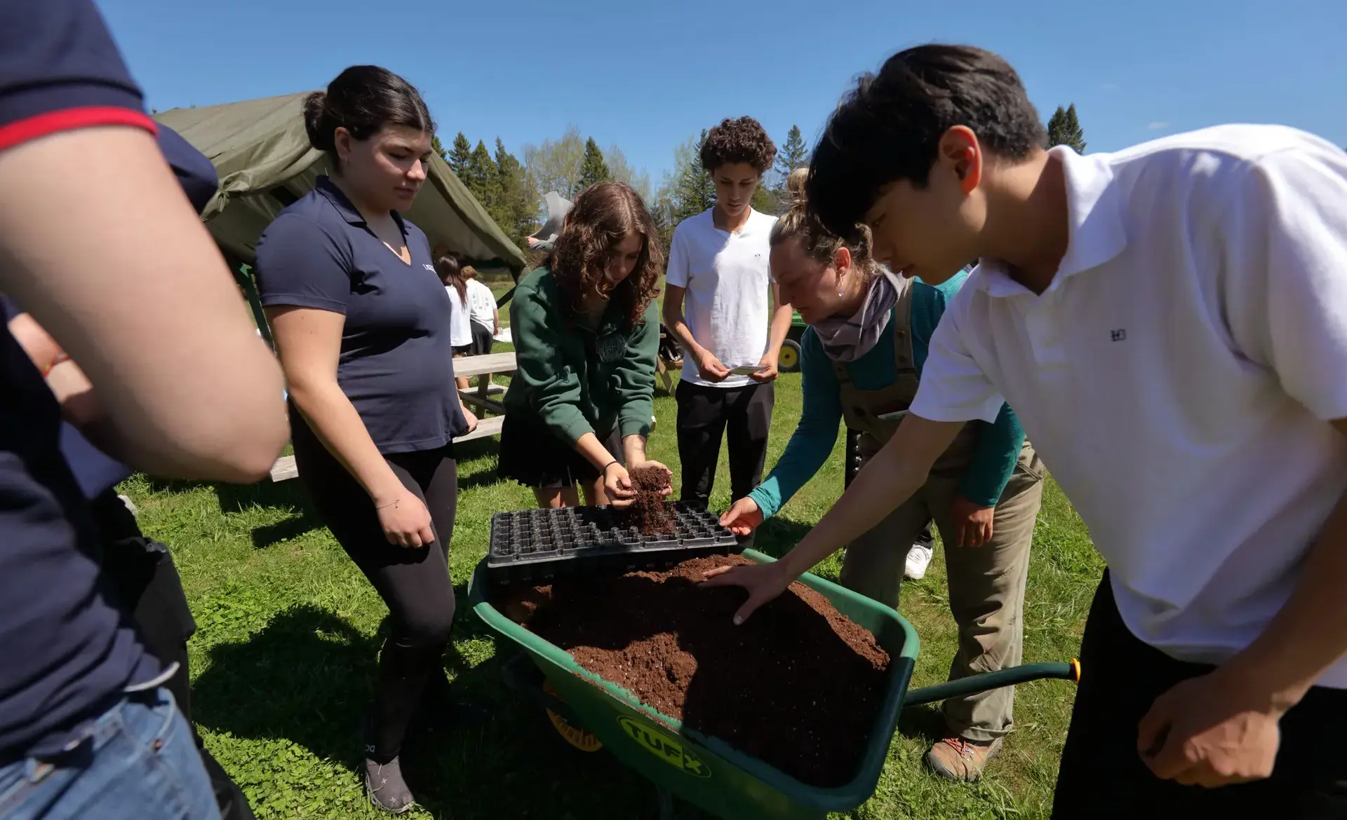 Students crowded round wheelbarrow filled with soil