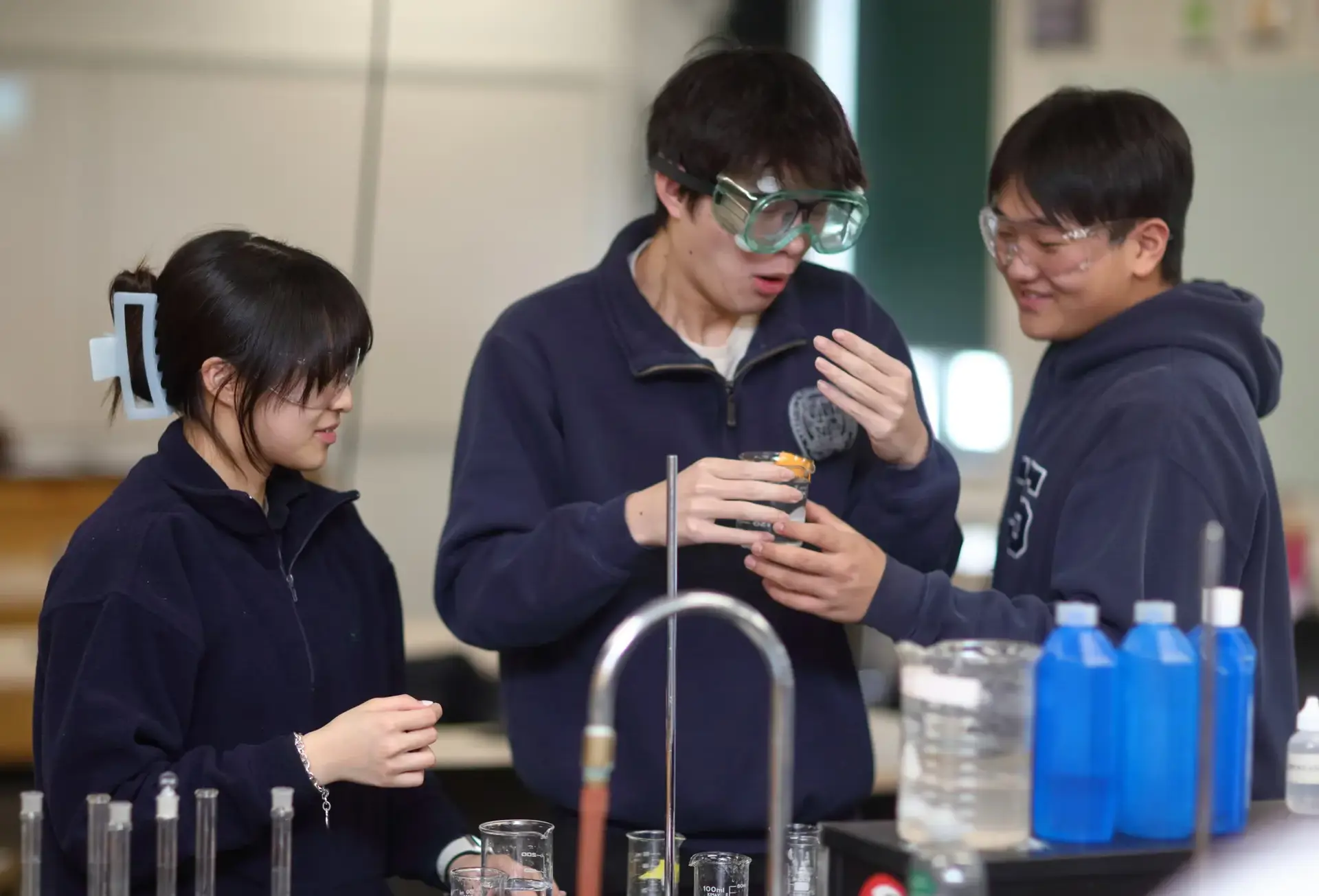 Three students wearing goggles in science lab