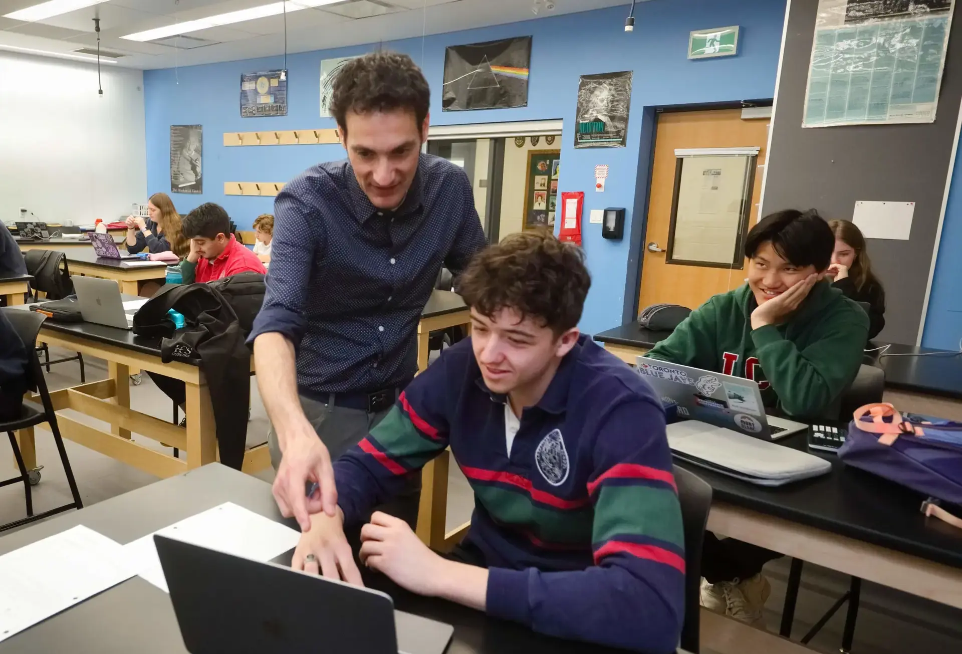 Teacher leaning over lab table, pointing at student's laptop