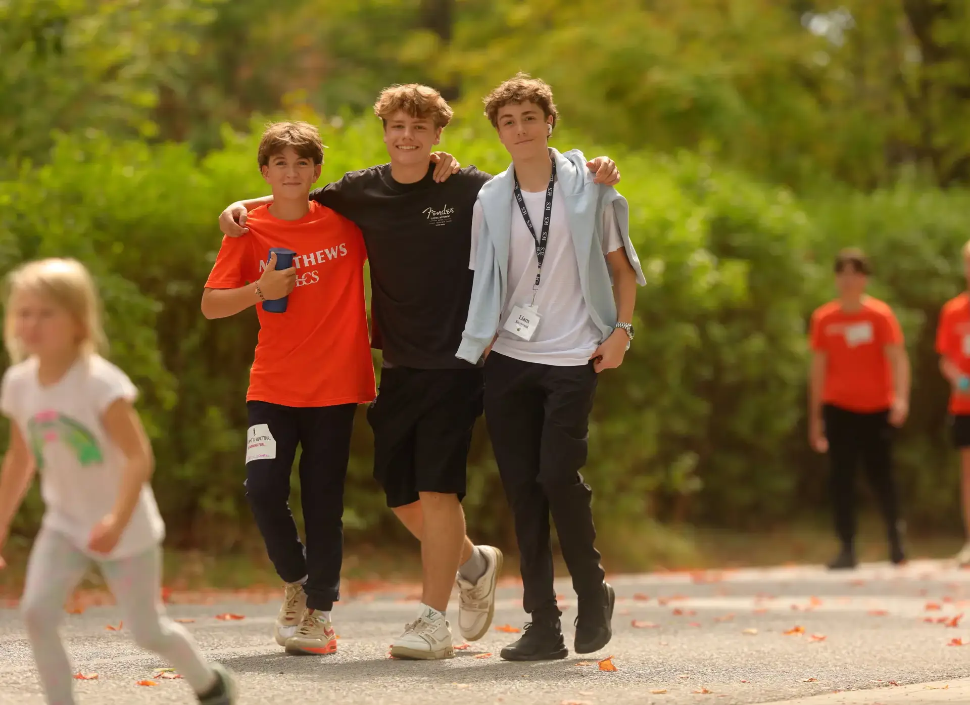Three male students walk arm-in-arm along a path during an outdoor event.