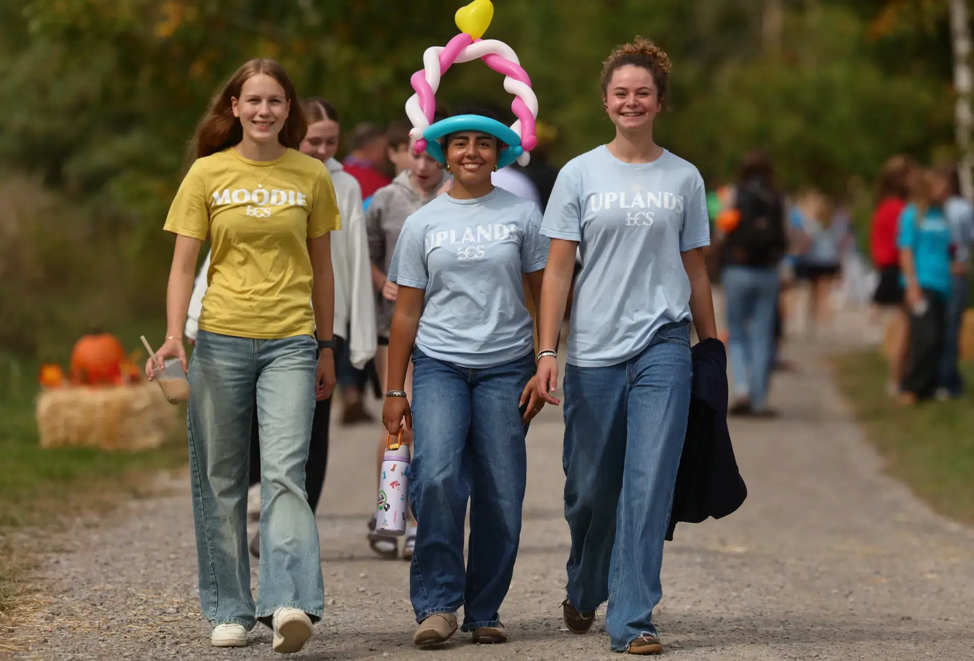 Three students walking up gravel path, one wearing a balloon hat