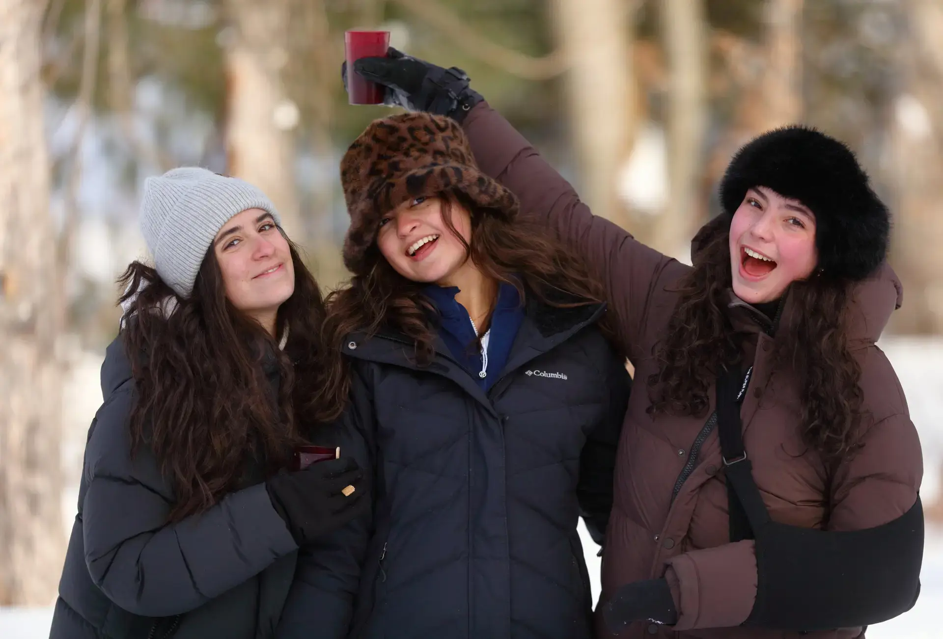 Three students in winterwear, one holding a cup above their head