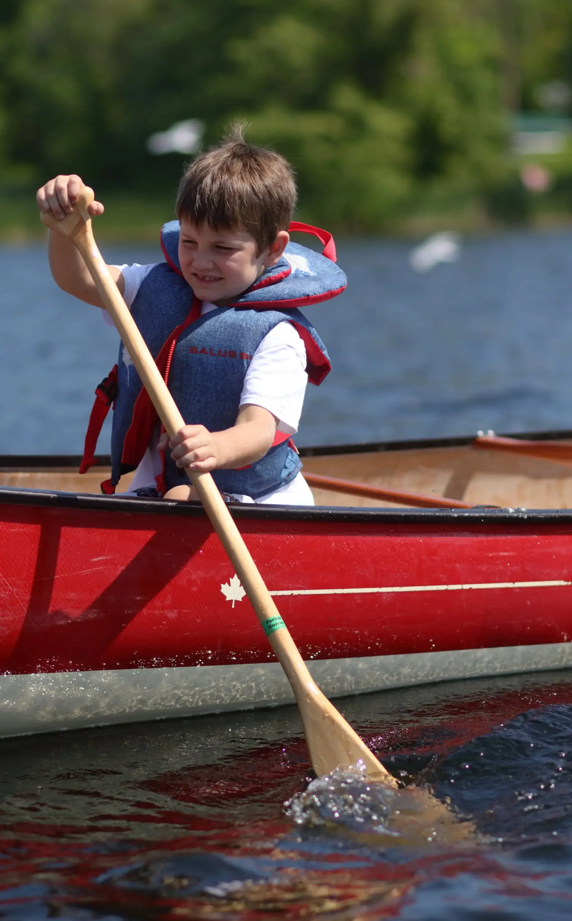 Camper wearing blue life preserver, rowing on lake